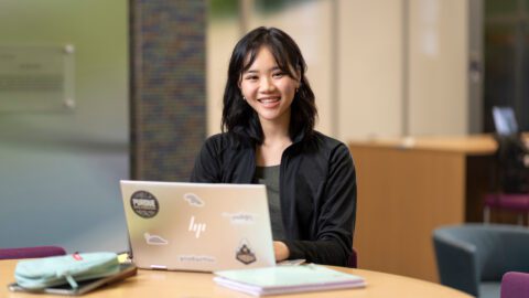 Britney Ho sits at a study table with laptop, smiling