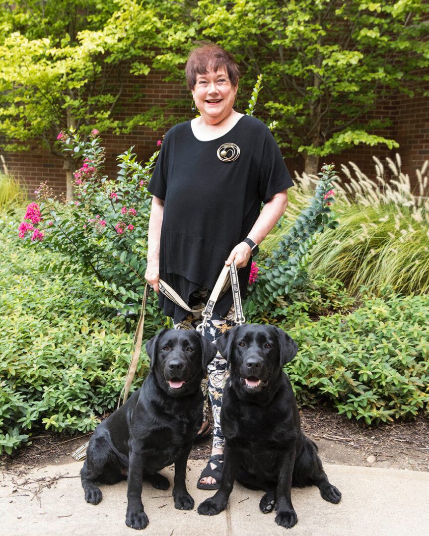 Two black labs — named Billie Sue and Brandy — sit in front of Joanne Troutner.