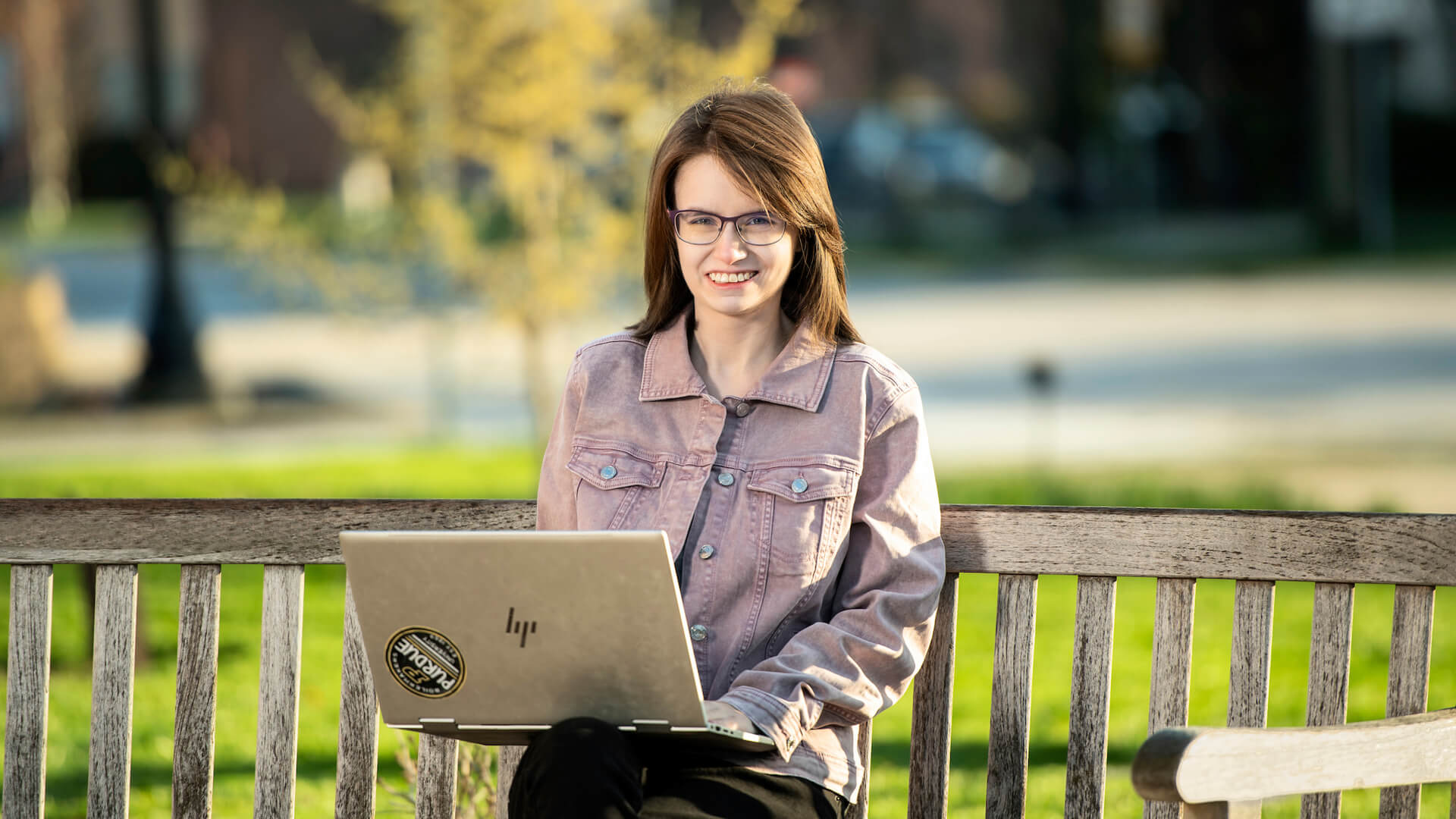 Grace sits on a bench at Horticulture Park with her laptop