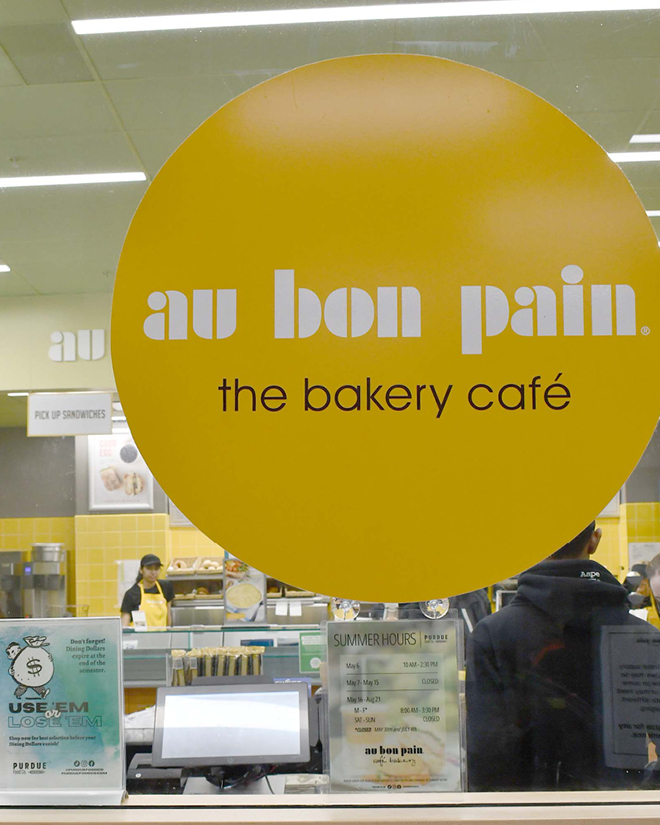 A photo of the logo of Au Bon Pain as well as a picture of the bright yellow café filled with students.