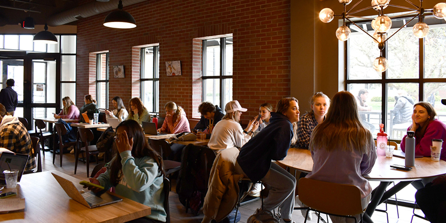 Students sit and talk at tables within Greyhouse.