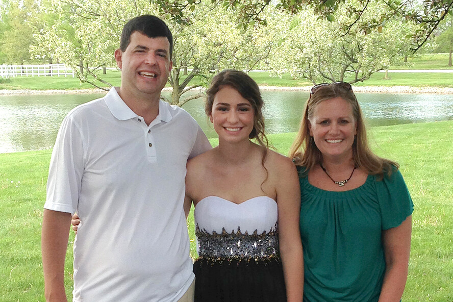 Madeline, in formal prom attire, poses with her parents.