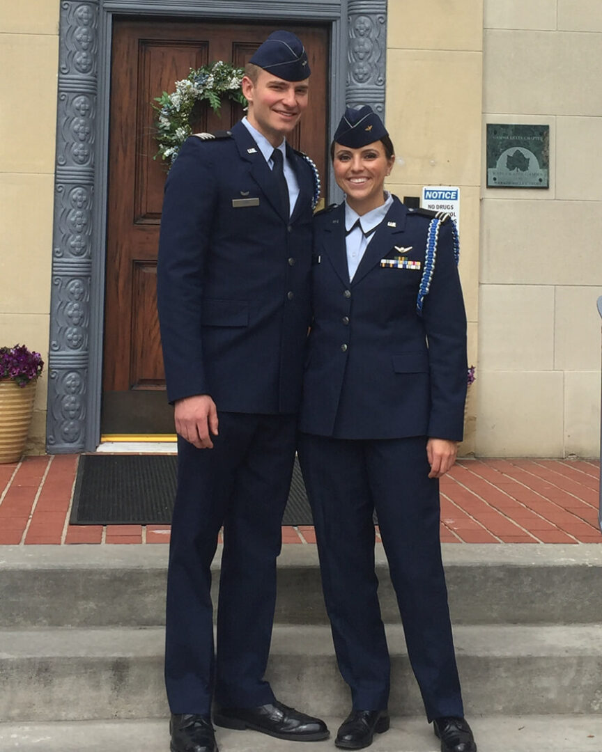 Ashley Bird and her husband, Brady Bird, stand in front of a door. They are both wearing their Air Force uniforms.