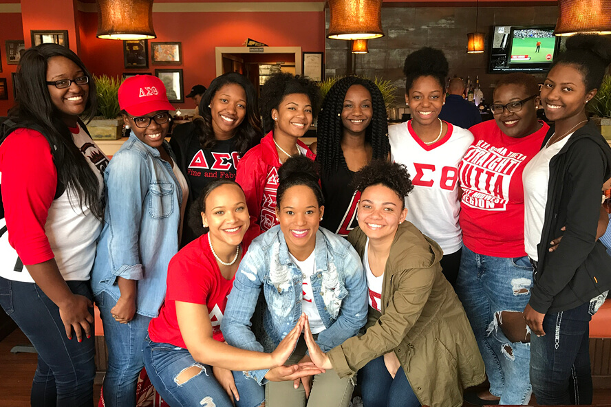 Eleven members of Delta Sigma Theta pose at a restaurant, three members in the front putting their hands together to create the shape of a Delta