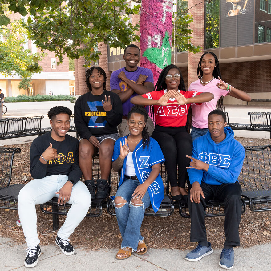 Seven students show their fraternity or sorority’s hand sign