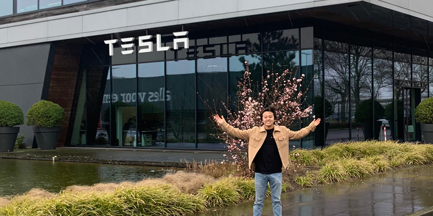 Nick poses, arms outspread, in front of the Tesla building