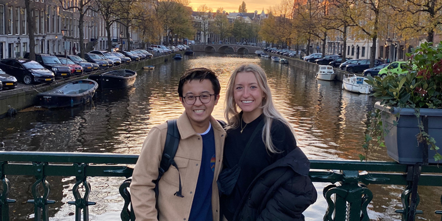 Nick poses on a bridge with a young woman, Amsterdam behind them