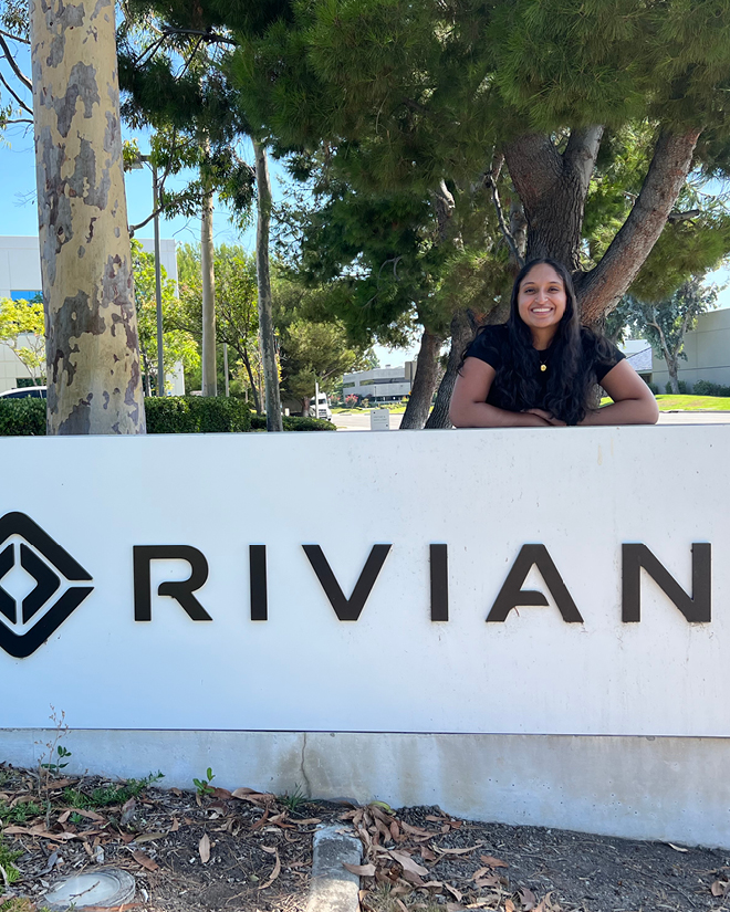 Pooja stands next to the Rivian sign