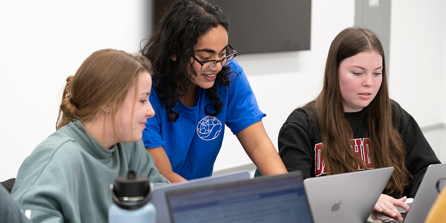 Reddy leans over two students to review a project on their laptops