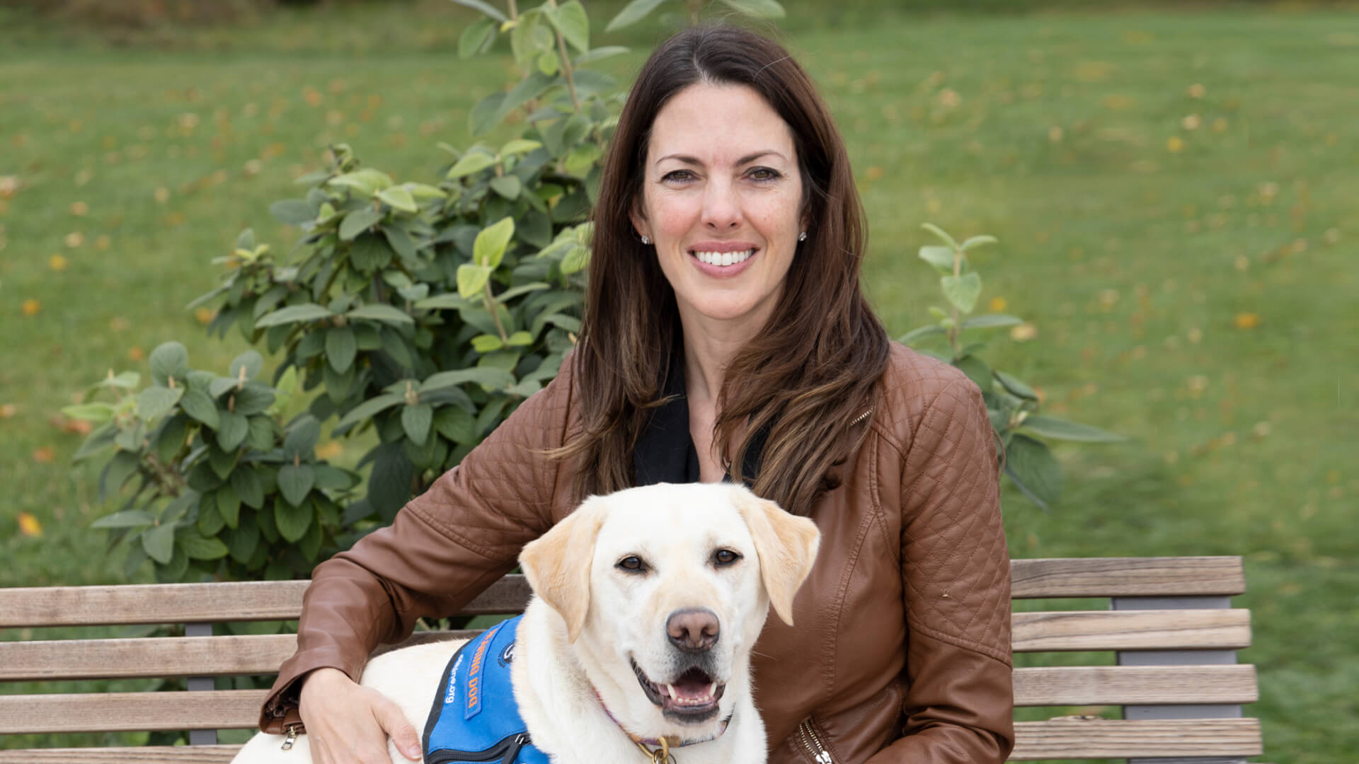 Dr. Michelle Ludwig poses on a bench, alongside her hearing service dog, Pam.