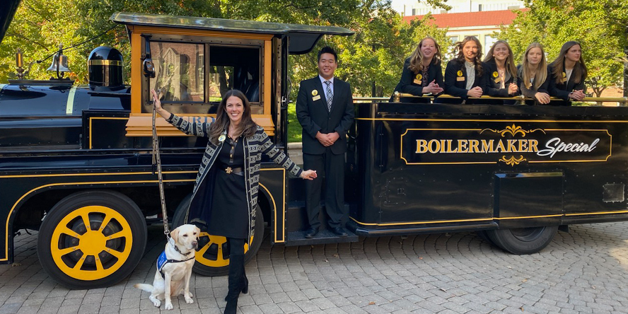 Dr. Ludwig poses next to the Boilermaker special, alongside her service dog, Pam, and students from the Old Masters program