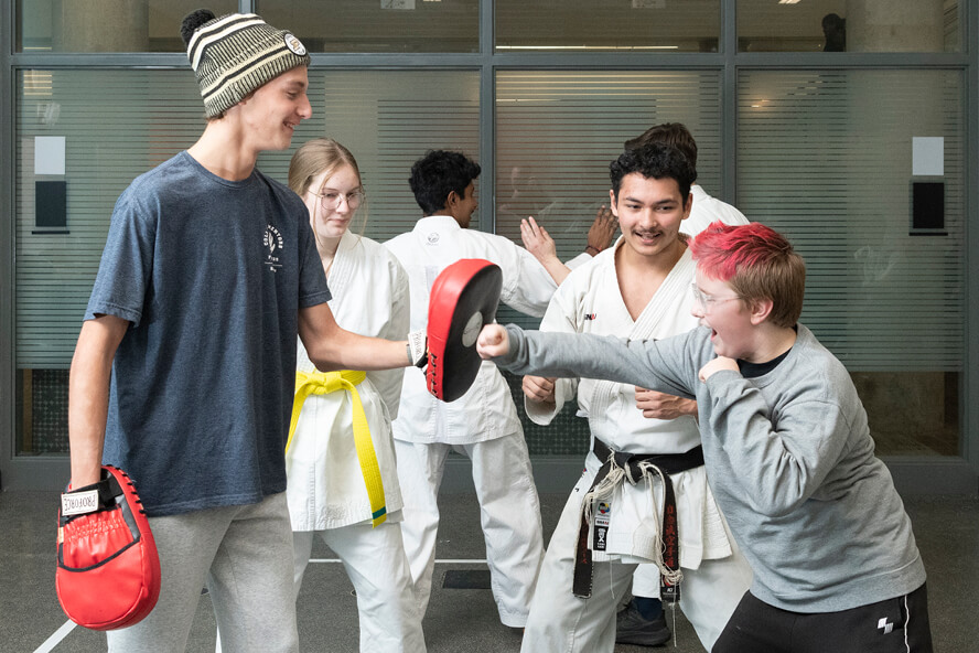 A martial arts instructor looks on as a student practices jabs, striking sparring pads held by Marciniak