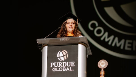 Lauren is delivering her speech, wearing a cap and gown and standing at the podium onstage.