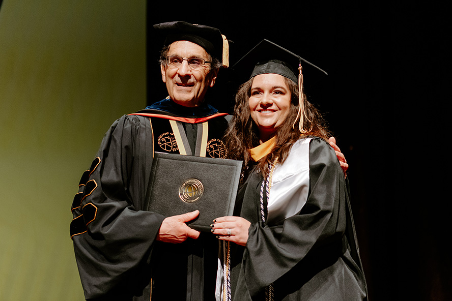 Dooley hands Lauren her diploma and, with his arm around her, they both smile for the camera.