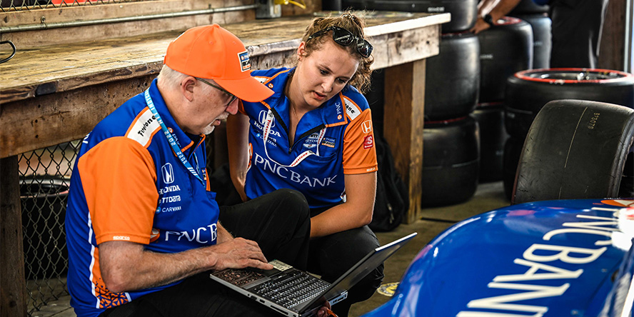 Hutton kneeling beside a colleague as they review performance data.