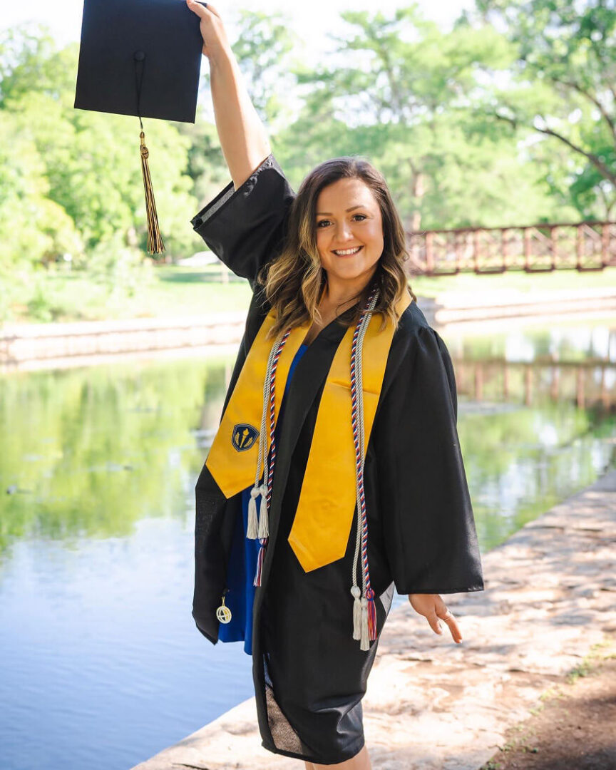 Finch wears her graduation gown, stole and cords, holding her cap in the air in a celebratory pose.