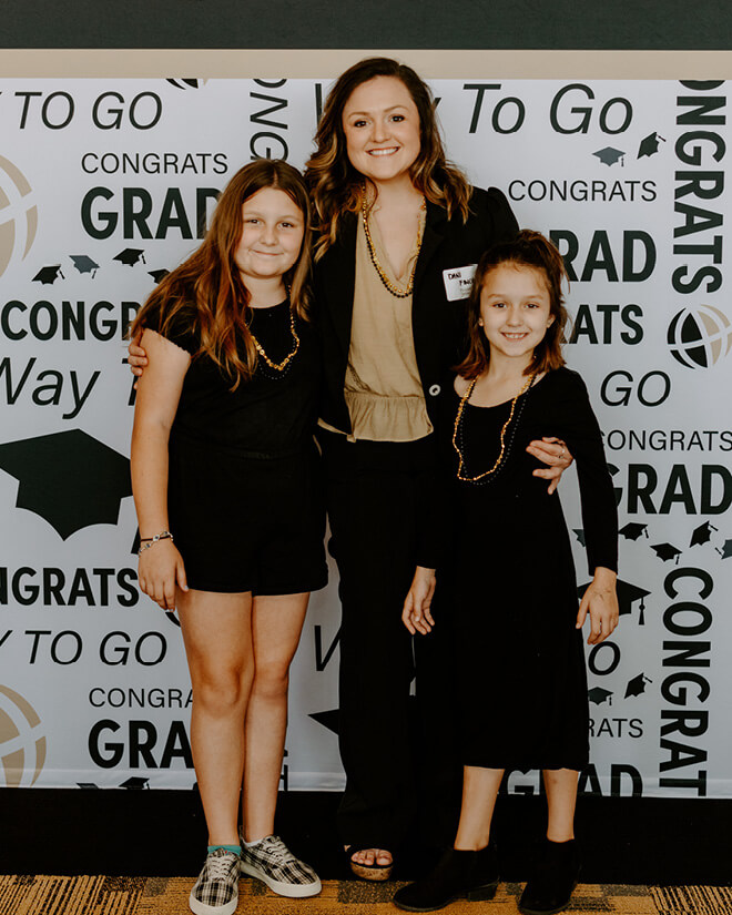 With a Purdue Global-branded congratulations banner behind them and dressed in black and gold, Finch poses with her two daughters. (Purdue University photo/Kelsey Lefever)