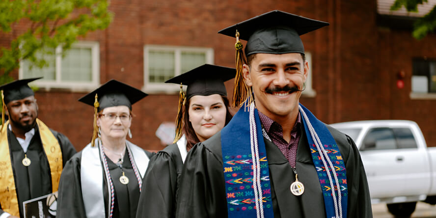 Juan smiles at the camera as he processes into Elliott Hall of Music, with three students behind him in line.