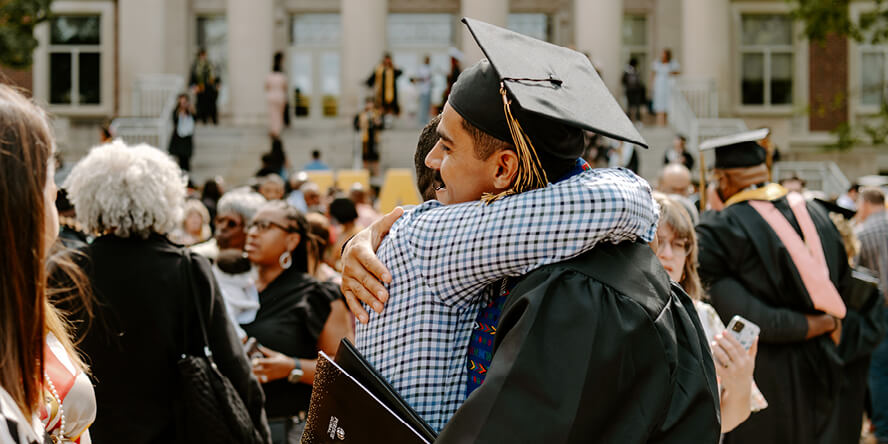With a crowd and the pillars of Hovde Hall behind them, Juan and his brother are hugging.