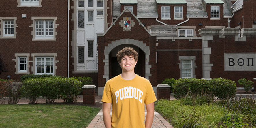 Kinder standing in front of Beta Theta House, a large red brick building. 