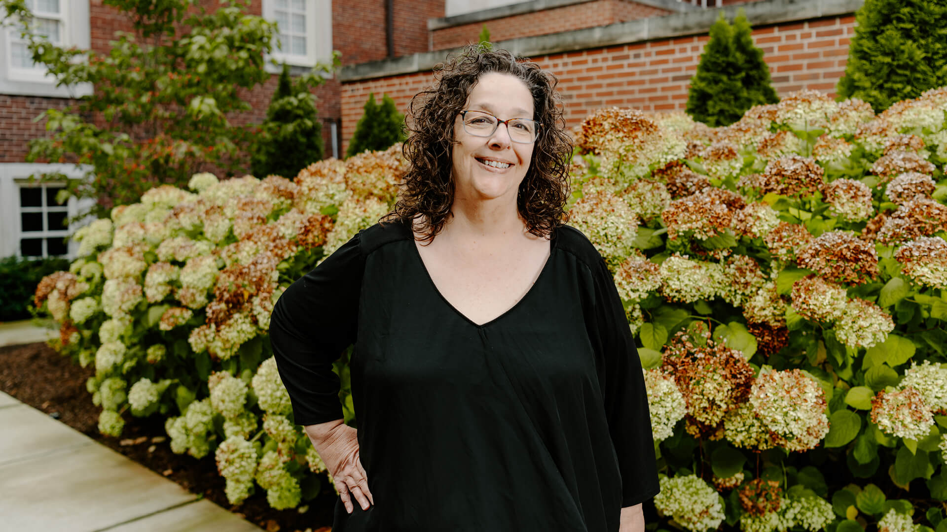 A woman with curly hair, glasses and a black shirt stands outside the Purdue Memorial Union.