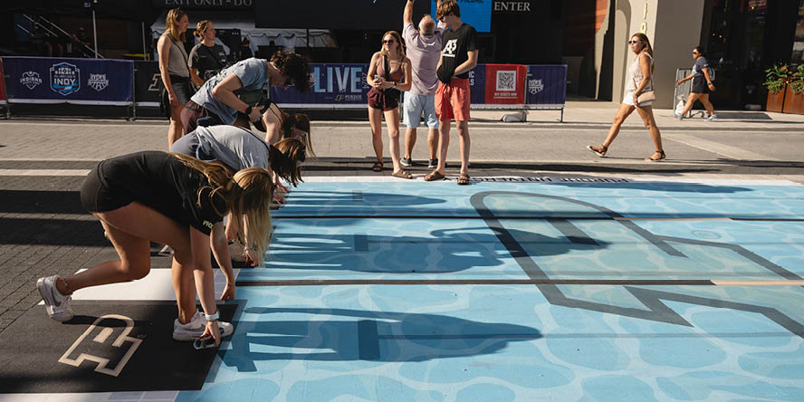 Four people leaning over a Purdue-branded swimming pool sidewalk graphic, people in background. 