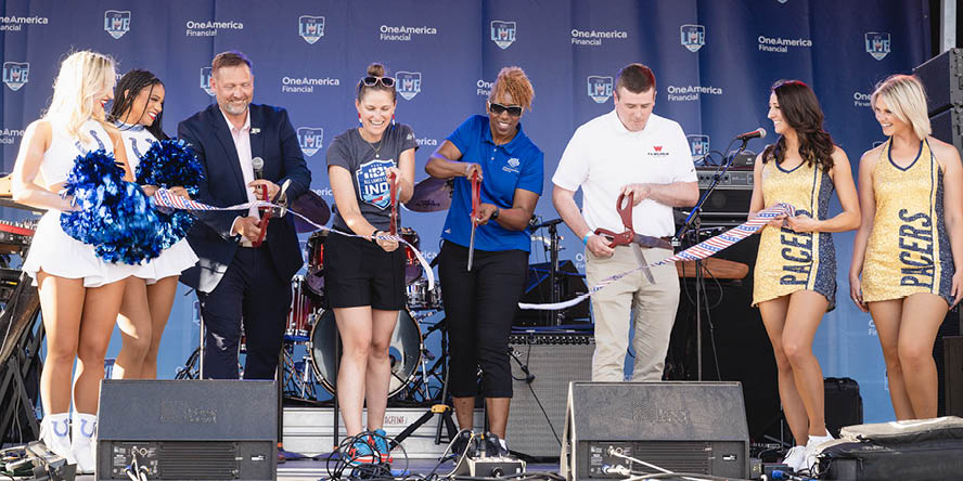 Eight people on a stage for a ribbon cutting ceremony.