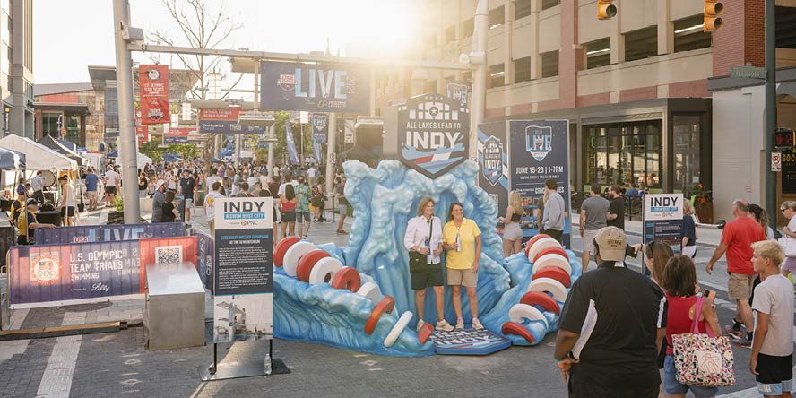 Crowd of people walking into the USA Swimming LIVE event with two people in the foreground standing in a blue wave 3D photo op. 