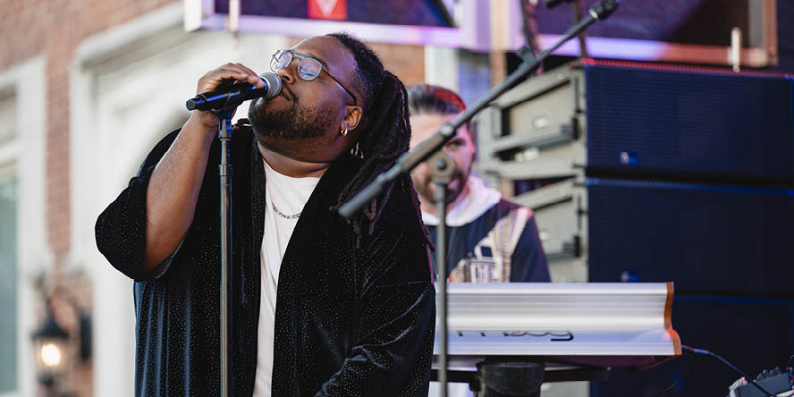 Man on stage singing into a microphone, keyboard player in background. 