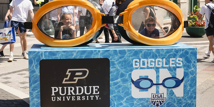 Two smiling children standing behind swimming goggles on a Purdue-branded 3D photo op. 