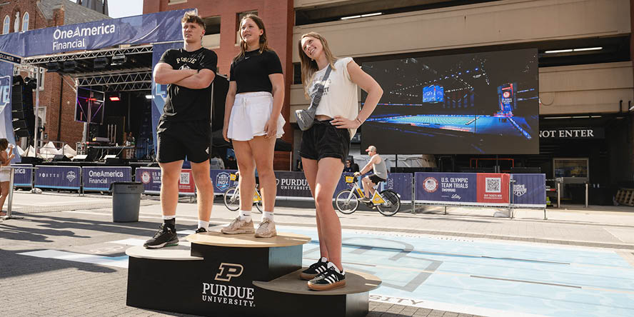 Three youths standing on a Purdue-branded awards podium, stage in background.