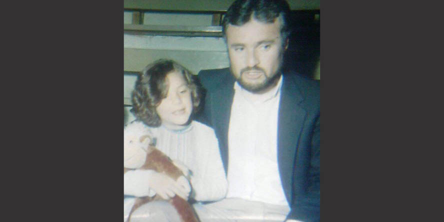 Palma, as a child, is pictured next to her dad, whose arm is around her. They’re both looking at something out of the frame and talking to each other.