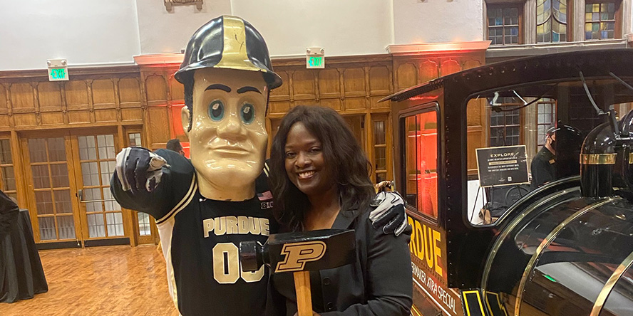 Desiré poses with Purdue Pete and his hammer next to the Boilermaker Special during commencement weekend. (Photo provided)
