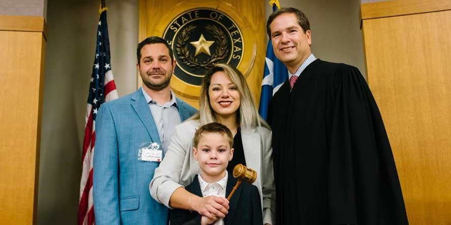 Nelly and her husband pose in a courthouse photo with their son and the judge. All four are smiling and Nelly is holding the judge’s gavel with the young boy.