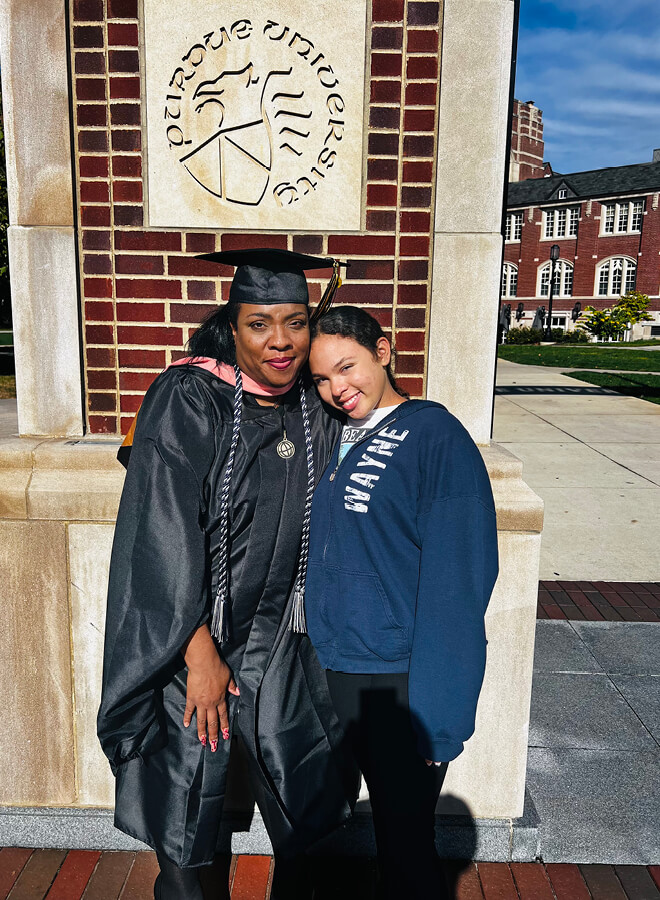 Victoria Durnell in her cap and gown with her daughter. The Purdue University seal is on the bricks behind them.  