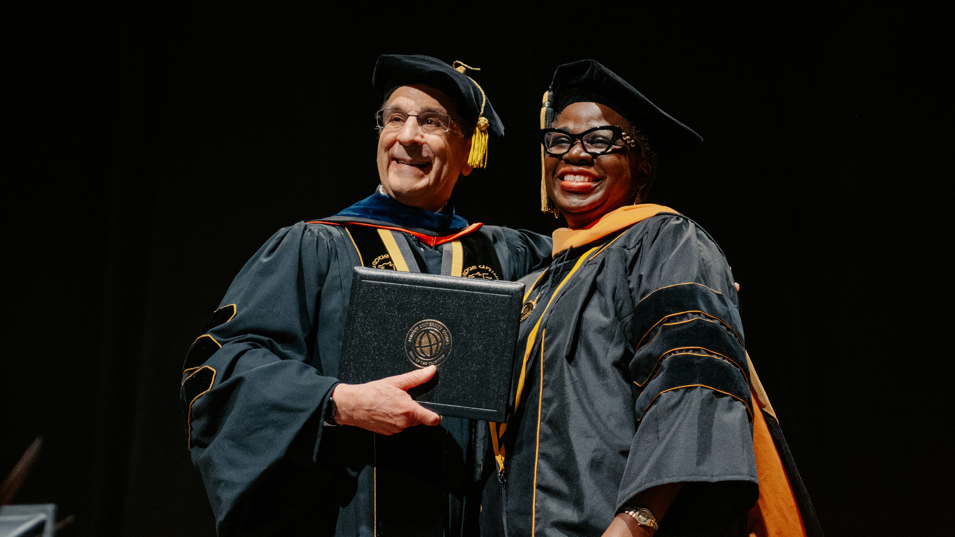 Sade Adeojo holds her diploma with Purdue Global Chancellor Frank Dooley at graduation.