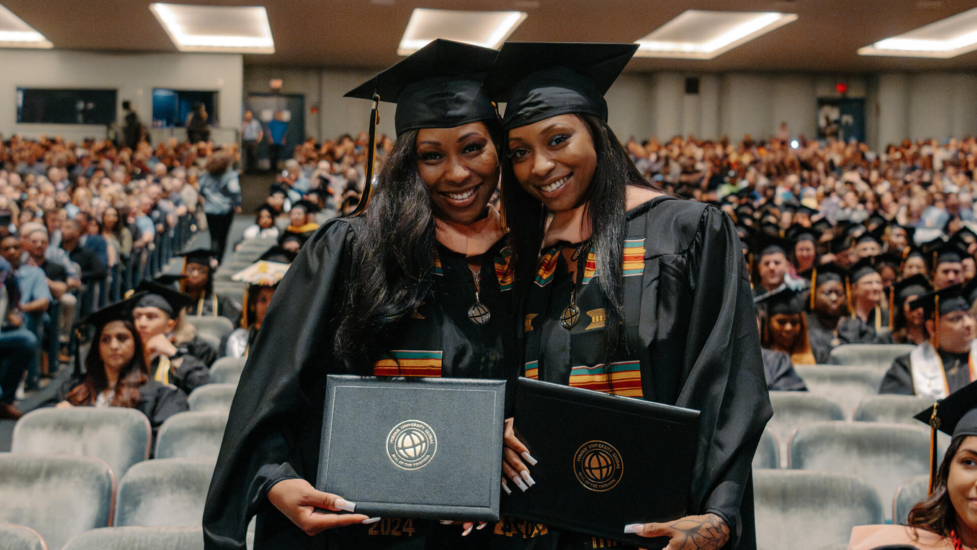 Chrishana and Chrishá Jackson stand next to each other, smiling and holding their degrees at graduation.