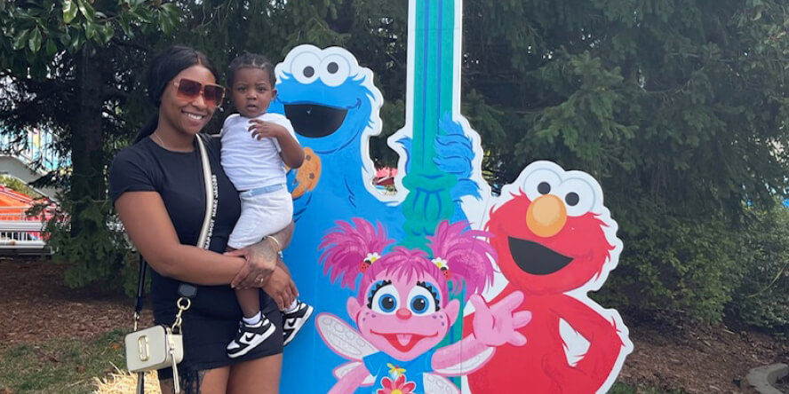 Chrishana Jackson holds her young son outside standing next to Sesame Street characters. 