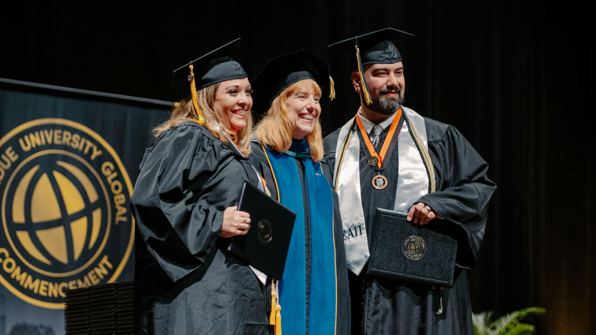 Rebecca and Caleb pose together on stage with their diplomas at their commencement ceremony.