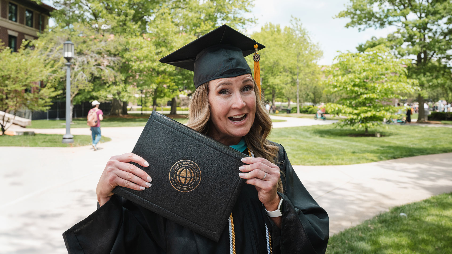 Patti Bertolino is wearing her cap and gown and holding up her diploma while laughing in triumph.