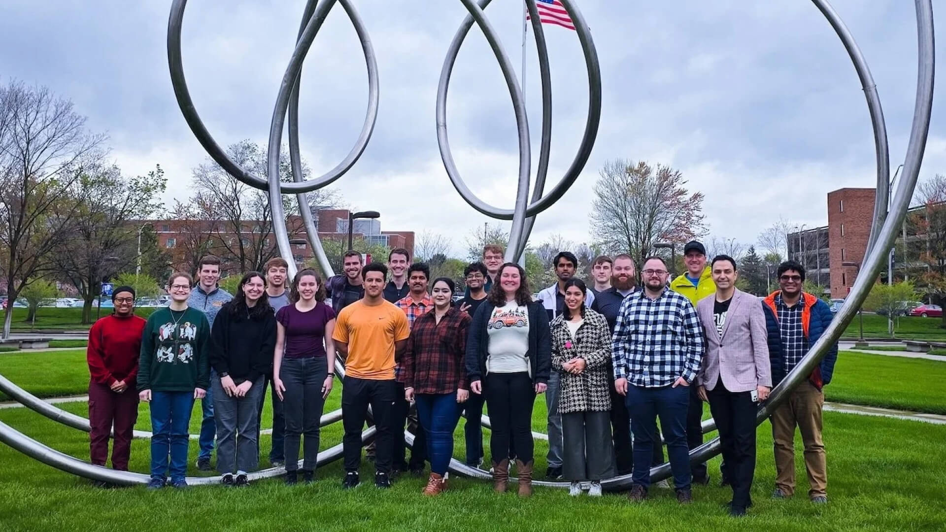 Group photo of people standing outside in front of a large, metal sculpture.