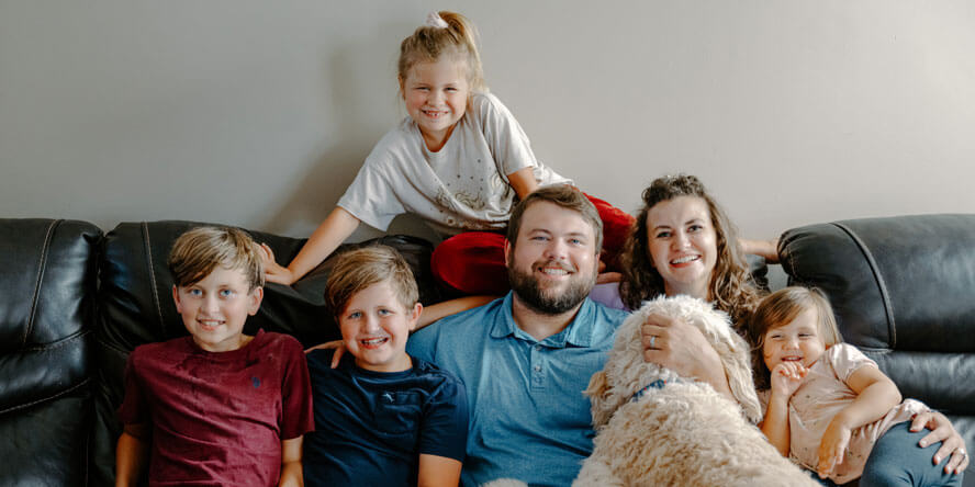 The Clawson family is pictured on their living room couch and George is climbing on Brendon. 