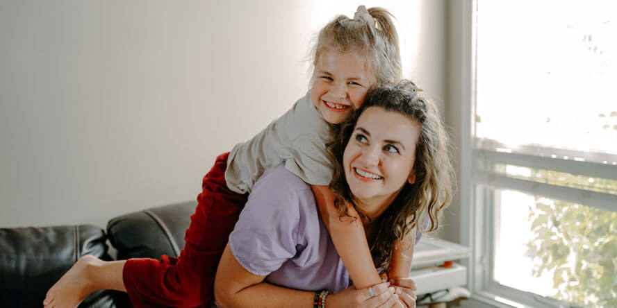 The oldest Clawson daughter is on her mom’s back, arms around her shoulders. Sienna turns her head toward her and smiles