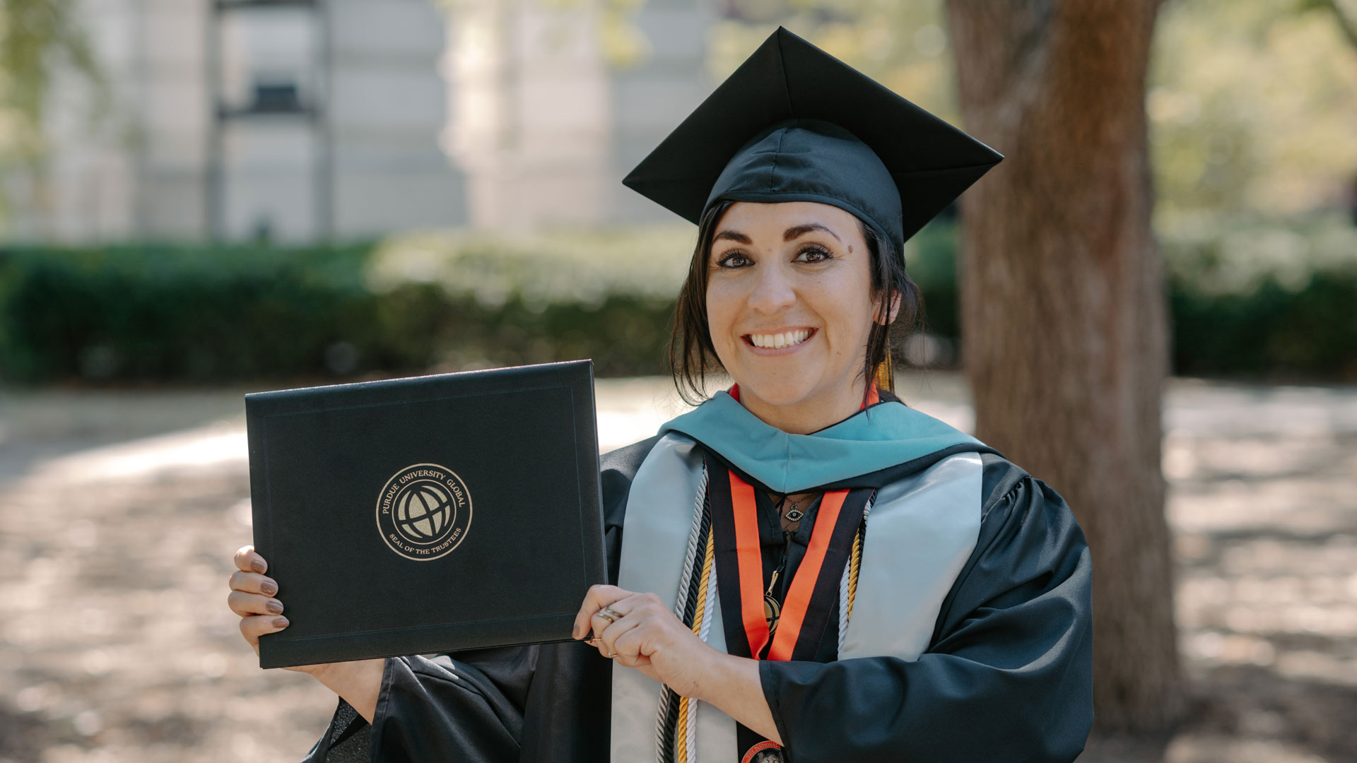 Yvette Martinez is wearing a cap and gown and holding up her diploma.