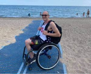 Kevin poses on a wheelchair ramp that leads to the water behind him. 