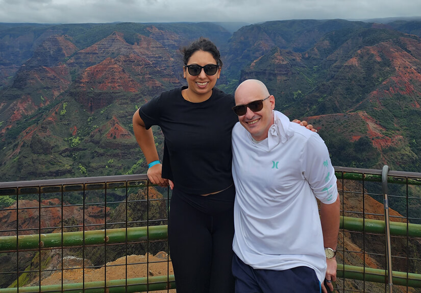 The couple poses in front of a fence, overlooking a stunning canyon.  