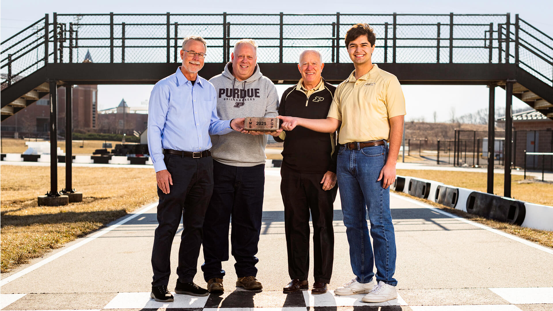 Purdue Grand Prix alums Al Wurster, Dave Fuhrman and Bill Shumaker hold up an Indianapolis Motor Speedway brick with Purdue Grand Prix Foundation president Wil Rohrbach.