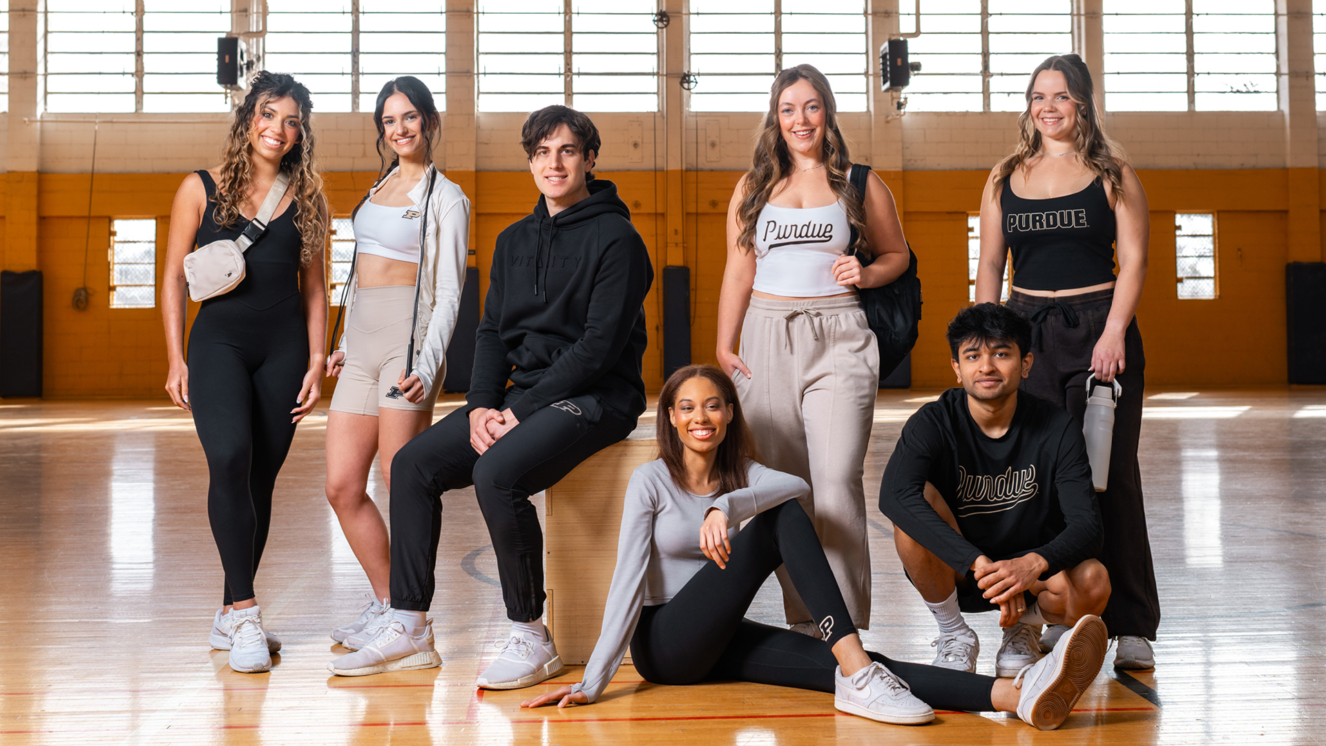 A group of students wearing the new Purdue x Vitality clothing smiling at the camera while posing inside of a gym.
