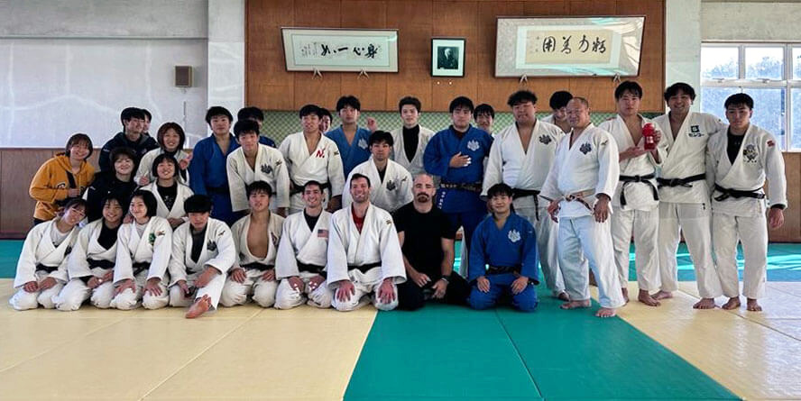 Kell Berliner poses at a dojo with a large group of fellow judokas.  