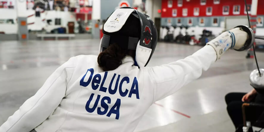 DeLuca is engaged in a bout with an unseen opponent, the back of her uniform visible, which reads “DeLuca USA”